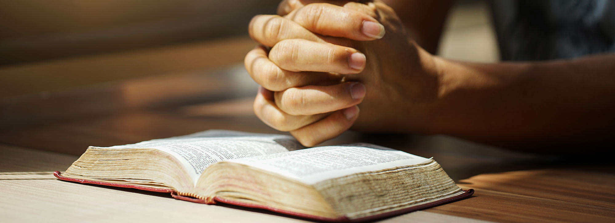 A person preying over a bible with clasped hands