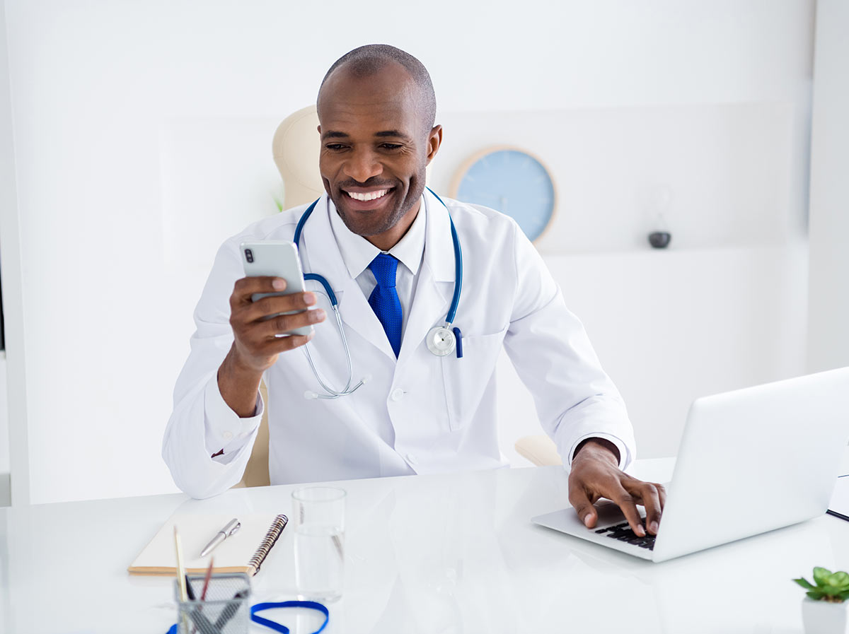 A family practice doctor uses his smartphone and laptop to manage his SMS services for healthcare